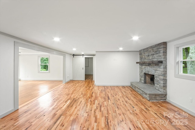 unfurnished living room with light wood finished floors, a barn door, a fireplace, and plenty of natural light