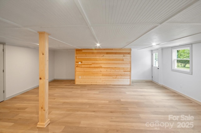 basement with light wood finished floors, wood walls, and baseboards