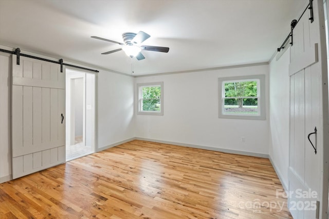 unfurnished bedroom with a barn door, wood finished floors, a ceiling fan, and baseboards