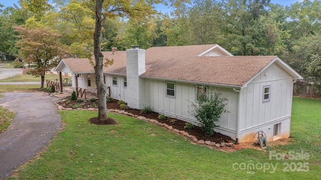 view of front of property with a chimney, aphalt driveway, roof with shingles, board and batten siding, and a front yard