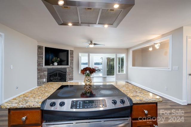 kitchen featuring dark wood-type flooring, island range hood, stainless steel range with electric cooktop, ceiling fan, and a fireplace