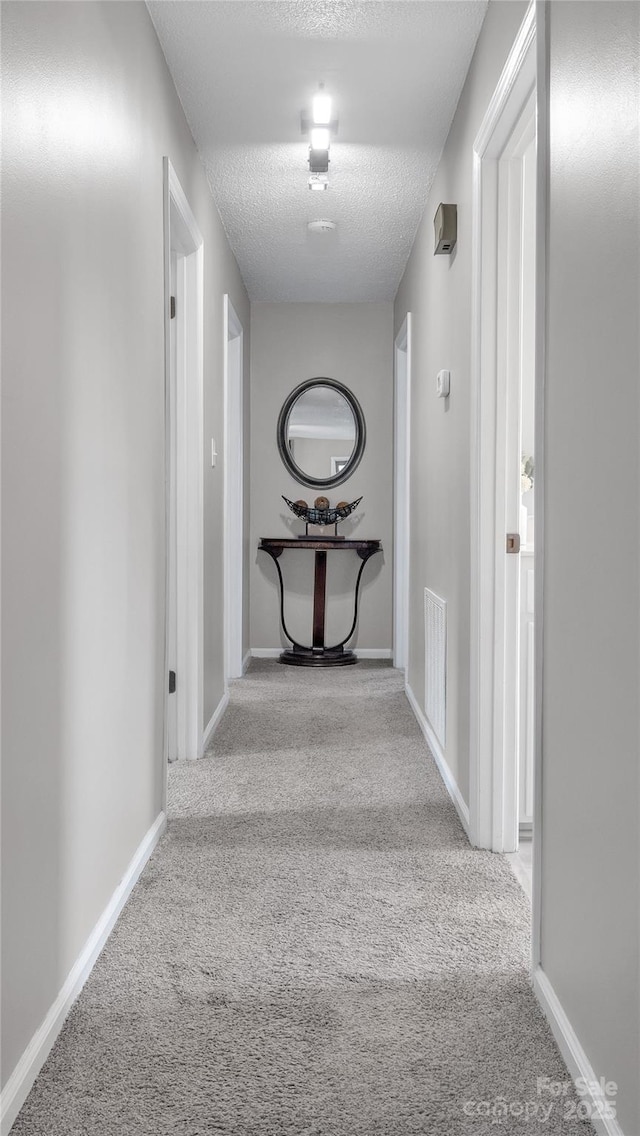 corridor with a textured ceiling and light colored carpet