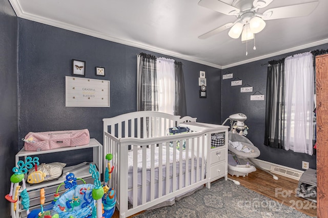 bedroom featuring ornamental molding, ceiling fan, a crib, and hardwood / wood-style flooring