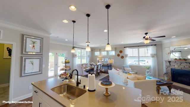 kitchen featuring white cabinets, a stone fireplace, sink, hanging light fixtures, and ceiling fan