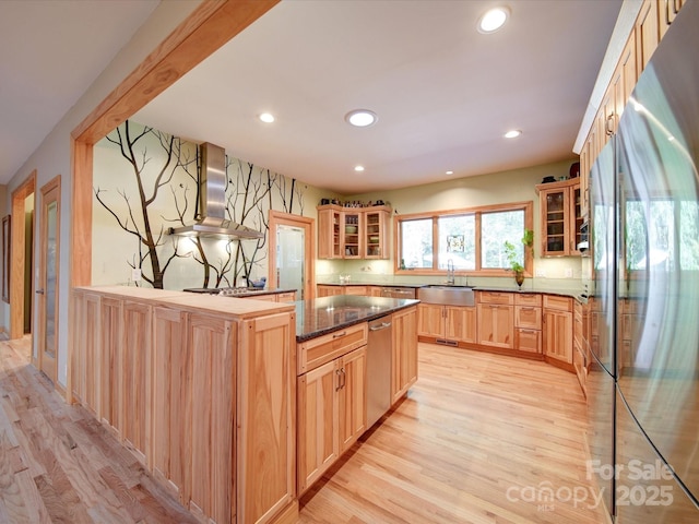 kitchen featuring glass insert cabinets, light brown cabinetry, appliances with stainless steel finishes, and wall chimney range hood