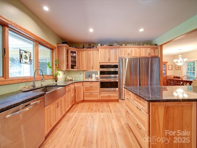 kitchen featuring light wood finished floors, glass insert cabinets, appliances with stainless steel finishes, light brown cabinetry, and a sink