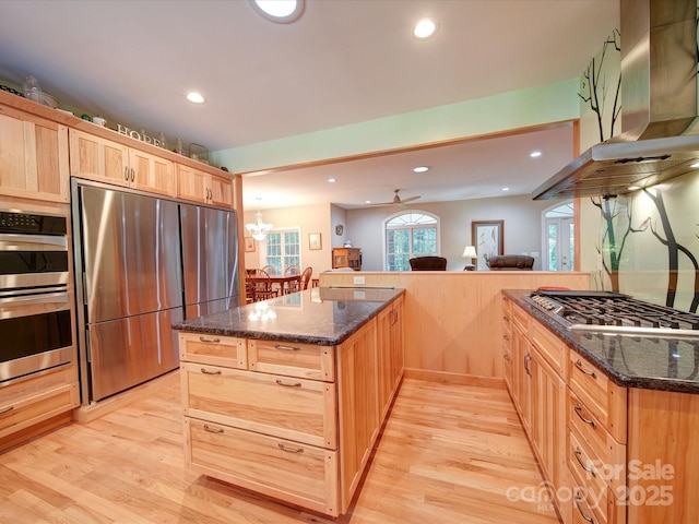 kitchen with light brown cabinets, island range hood, light wood-style floors, appliances with stainless steel finishes, and dark stone counters