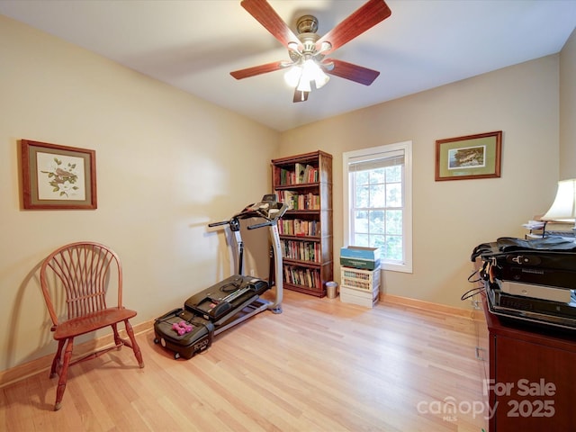 exercise room featuring light wood-type flooring, a ceiling fan, and baseboards