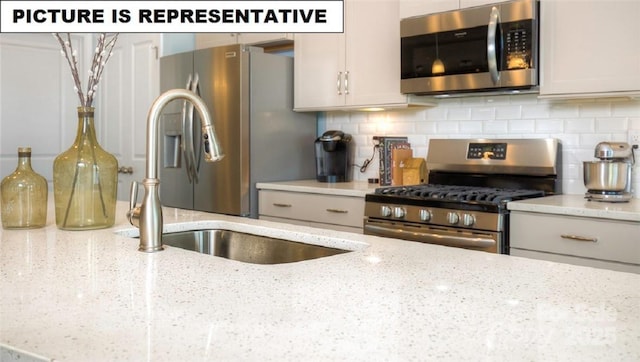 kitchen with white cabinetry, appliances with stainless steel finishes, backsplash, and light stone counters