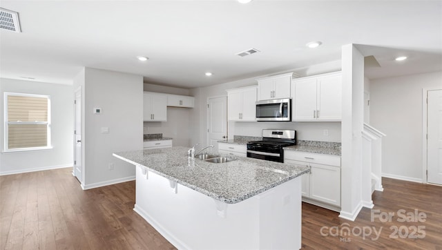 kitchen featuring an island with sink, appliances with stainless steel finishes, dark wood-style flooring, white cabinetry, and a sink