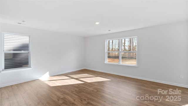 empty room with wood finished floors, visible vents, and baseboards