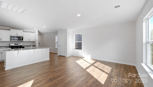 kitchen with a kitchen island with sink, stainless steel appliances, dark wood-type flooring, a breakfast bar, and white cabinets