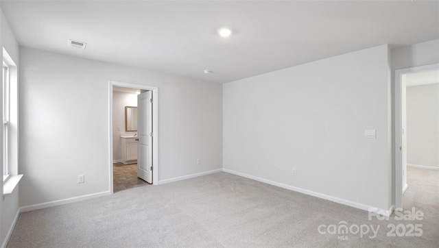 unfurnished bedroom featuring baseboards, ensuite bathroom, visible vents, and light colored carpet