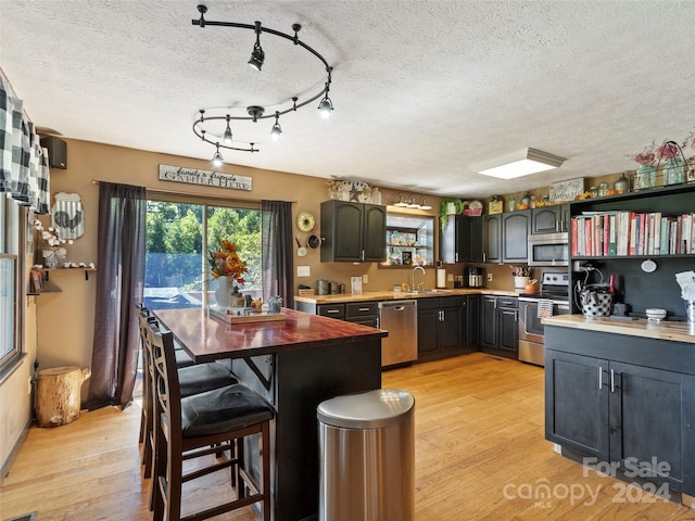 kitchen featuring sink, a textured ceiling, light hardwood / wood-style floors, a kitchen bar, and stainless steel appliances