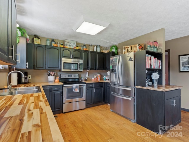 kitchen with wooden counters, light wood-type flooring, a textured ceiling, stainless steel appliances, and sink