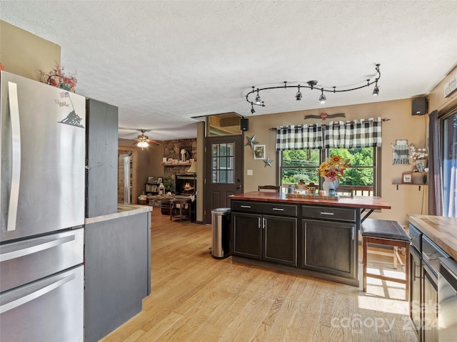 kitchen featuring stainless steel fridge, a textured ceiling, ceiling fan, a fireplace, and light hardwood / wood-style floors