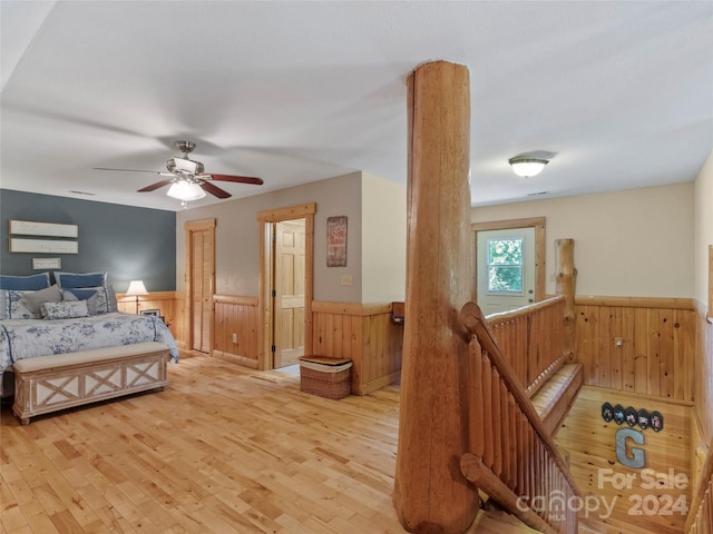 bedroom featuring ceiling fan, light hardwood / wood-style flooring, and wood walls