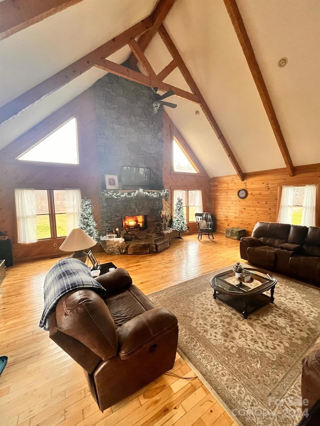 living room with light hardwood / wood-style floors, a stone fireplace, ceiling fan, and a healthy amount of sunlight