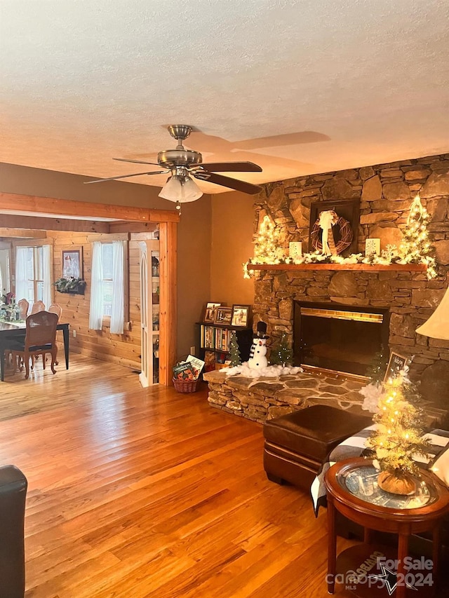 living room with ceiling fan, a fireplace, a textured ceiling, and light wood-type flooring