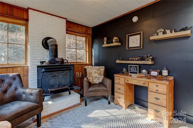 living area featuring crown molding, wood walls, a wood stove, and a wealth of natural light