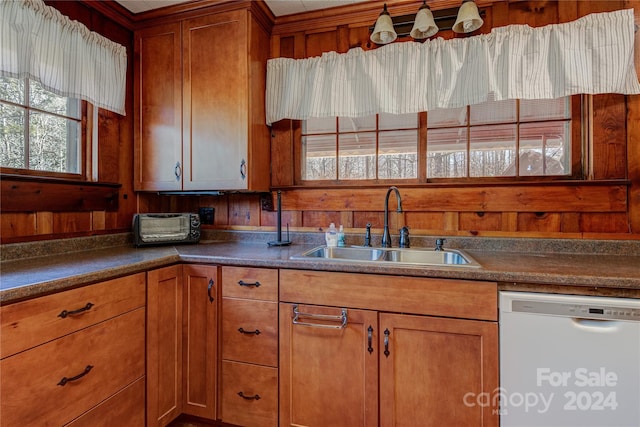 kitchen with white dishwasher, wood walls, and sink