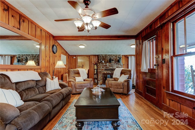 living room with a fireplace, beamed ceiling, ceiling fan, light hardwood / wood-style flooring, and wooden walls