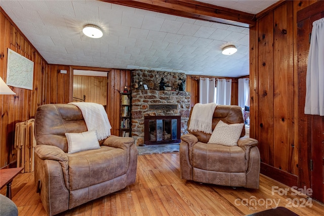 living room featuring light wood-type flooring, beam ceiling, a fireplace, and wooden walls