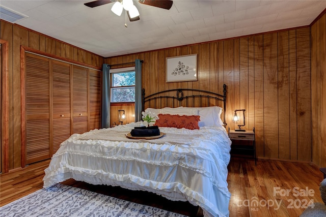 bedroom with ceiling fan, wood walls, and wood-type flooring