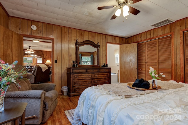 bedroom featuring wooden walls, ensuite bath, ceiling fan, and hardwood / wood-style floors