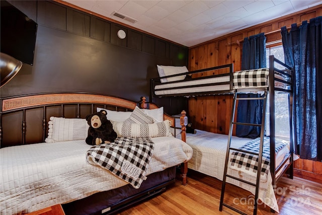 bedroom with crown molding, wooden walls, and light hardwood / wood-style flooring