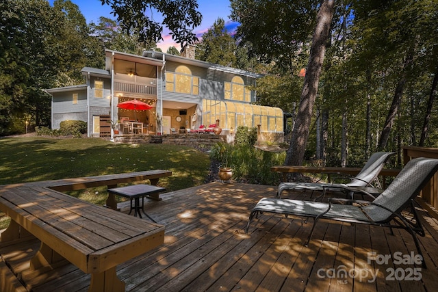 back house at dusk with a sunroom, a yard, and a deck