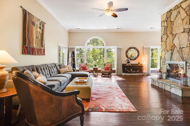 living room with ceiling fan, ornamental molding, a stone fireplace, and dark hardwood / wood-style flooring