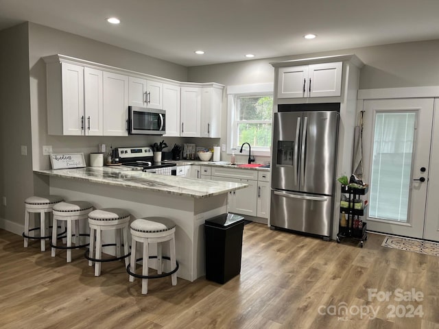 kitchen with light stone countertops, a kitchen bar, kitchen peninsula, white cabinetry, and stainless steel appliances