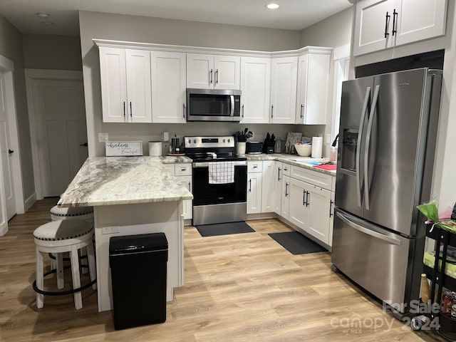 kitchen with light stone countertops, light wood-type flooring, a kitchen breakfast bar, white cabinetry, and stainless steel appliances