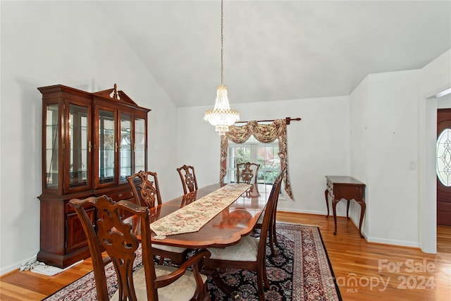 dining area with wood-type flooring, an inviting chandelier, and lofted ceiling