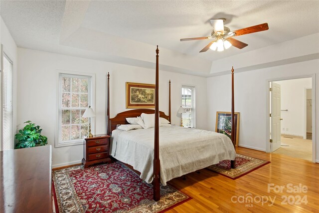 bedroom with ensuite bathroom, a textured ceiling, a tray ceiling, ceiling fan, and hardwood / wood-style flooring