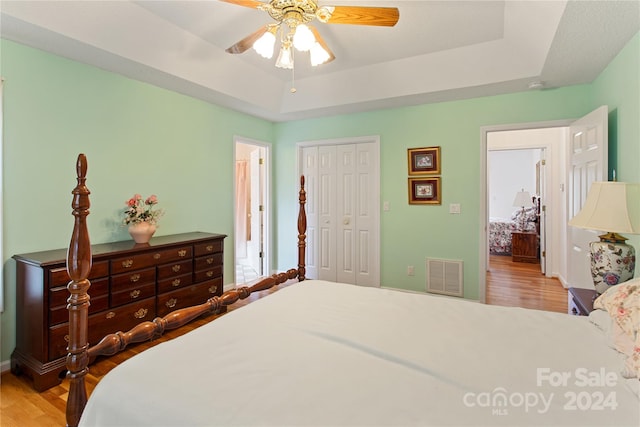 bedroom with ceiling fan, a raised ceiling, wood-type flooring, and a closet