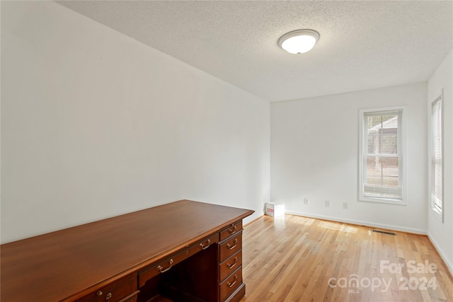 unfurnished office featuring light hardwood / wood-style floors and a textured ceiling