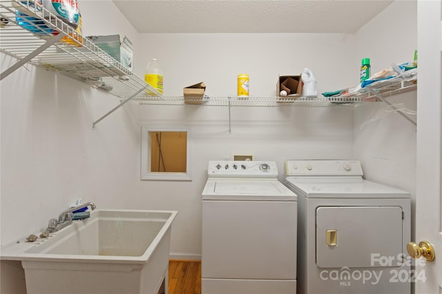 clothes washing area featuring a textured ceiling, hardwood / wood-style flooring, washer and clothes dryer, and sink