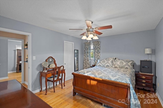 bedroom with a textured ceiling, ceiling fan, and light hardwood / wood-style floors