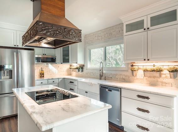 kitchen featuring premium range hood, white cabinetry, stainless steel appliances, a center island, and light stone countertops