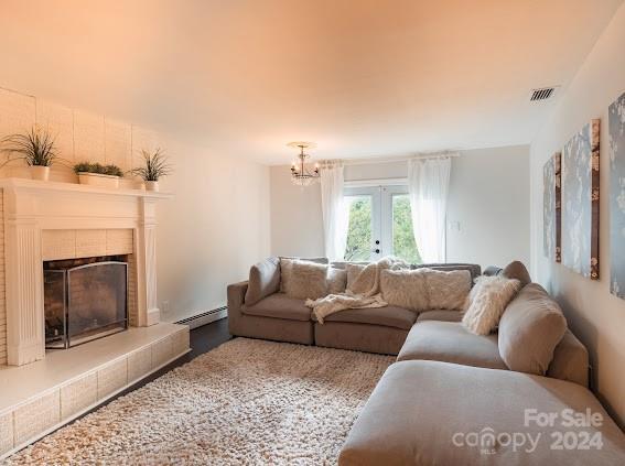 living room with a notable chandelier, a baseboard heating unit, a tile fireplace, and french doors