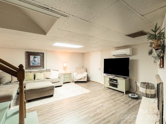 living room with lofted ceiling, an AC wall unit, a drop ceiling, and hardwood / wood-style flooring