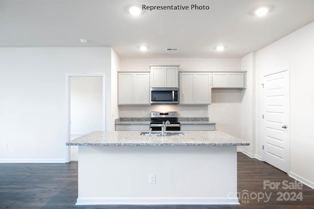 kitchen with stainless steel appliances, sink, light stone countertops, dark hardwood / wood-style floors, and a center island with sink