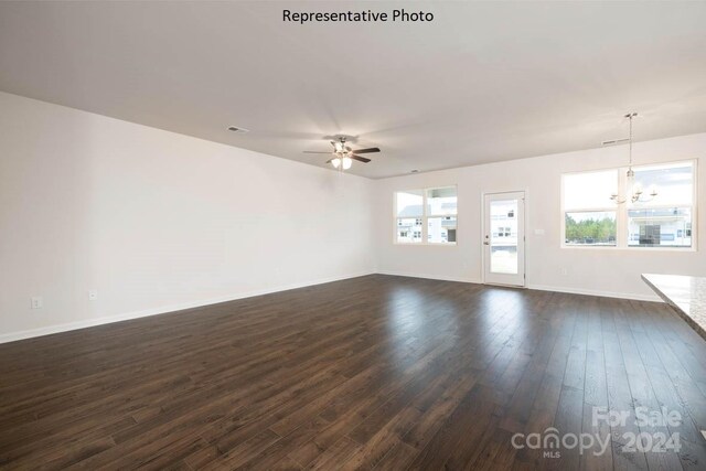 unfurnished living room with ceiling fan with notable chandelier and dark wood-type flooring