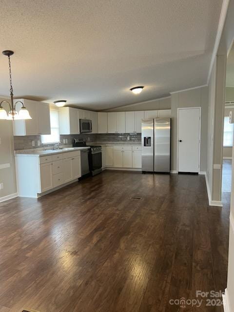 kitchen with stainless steel appliances, vaulted ceiling, pendant lighting, white cabinets, and dark hardwood / wood-style floors