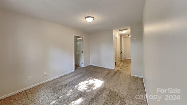 spare room featuring a textured ceiling and light colored carpet