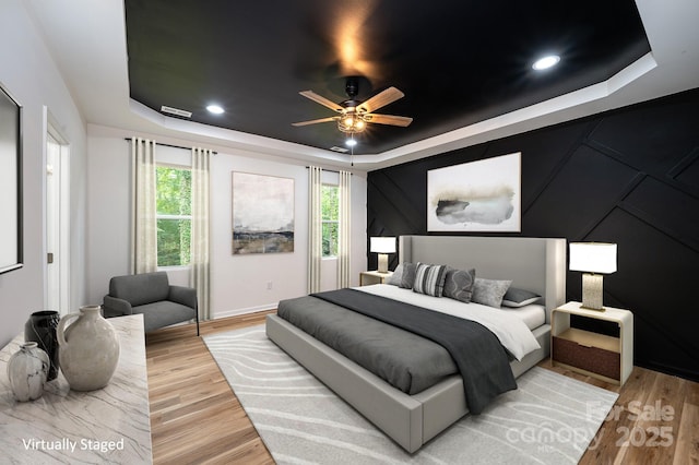 bedroom featuring recessed lighting, a raised ceiling, and light wood-style floors