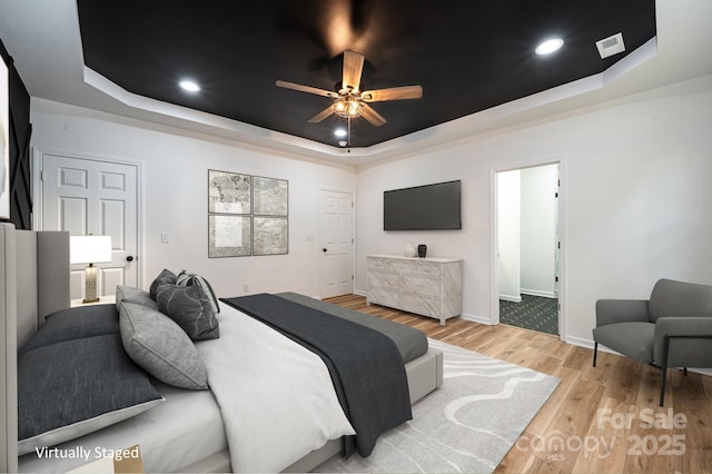 bedroom with baseboards, visible vents, a raised ceiling, wood finished floors, and recessed lighting