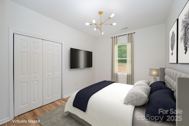 bedroom featuring visible vents, baseboards, light wood-style floors, a chandelier, and a closet